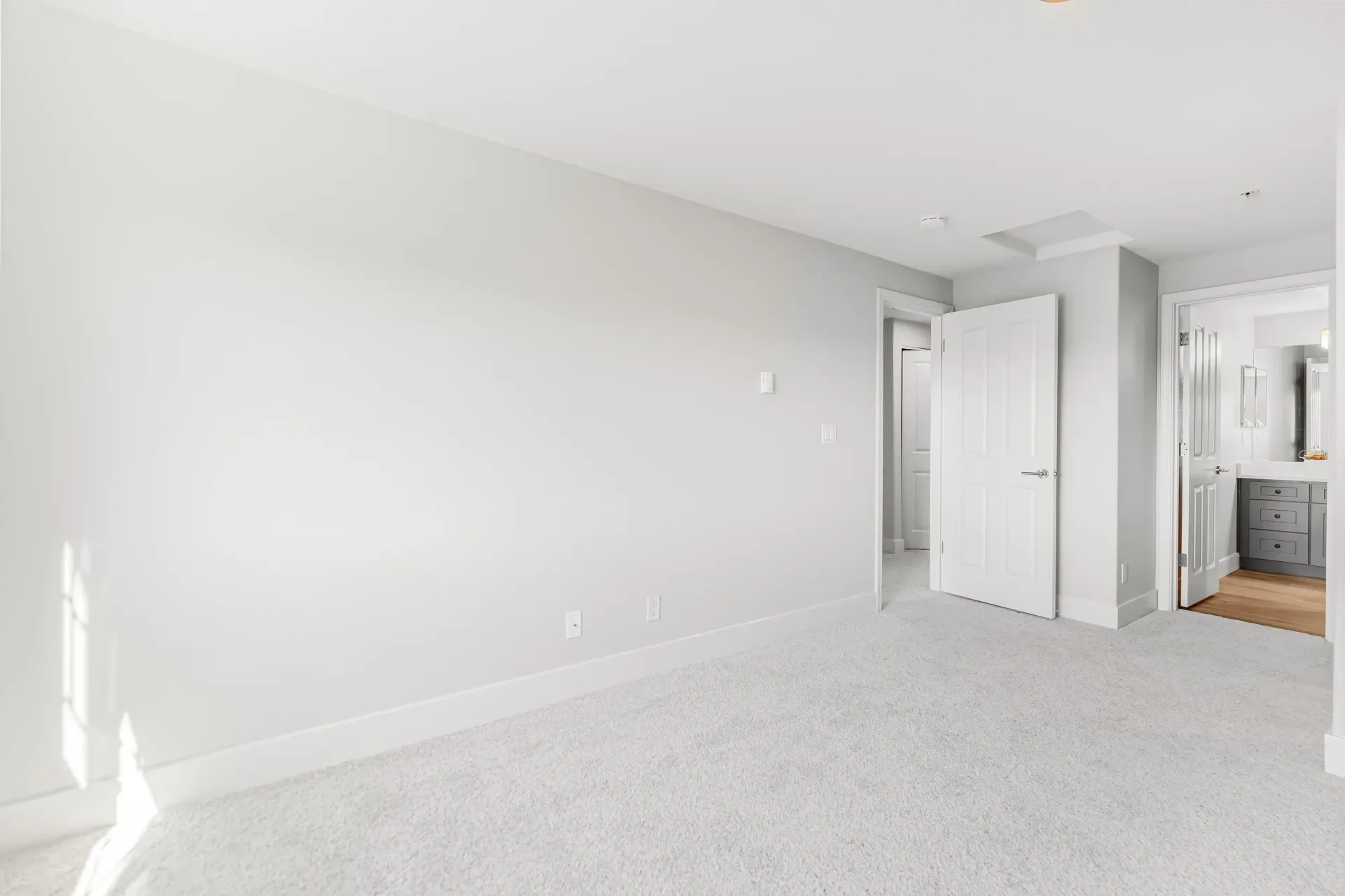 Empty bedroom with light gray walls, white trim, and a door to a bathroom.