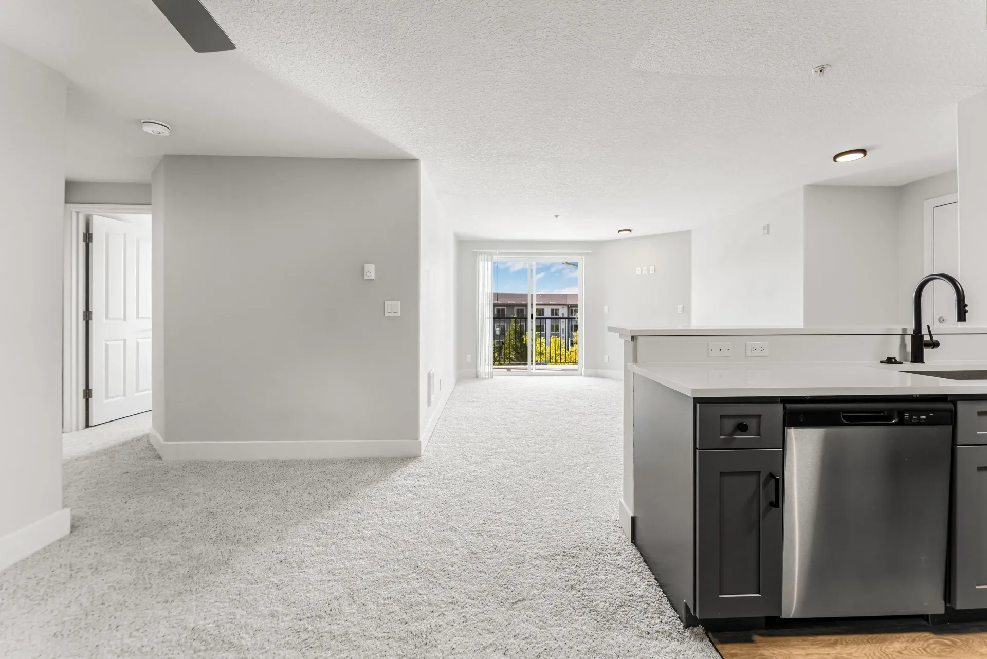Open-concept apartment interior with kitchen island, stainless appliances, and balcony door.
