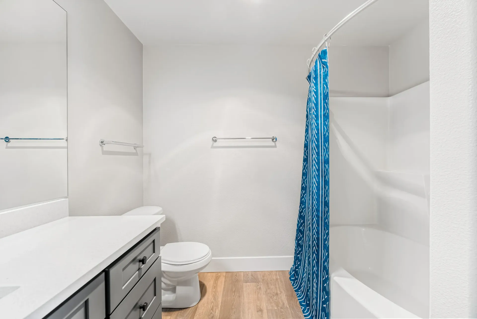Bathroom with vanity, toilet, and a shower-tub with a blue patterned curtain.