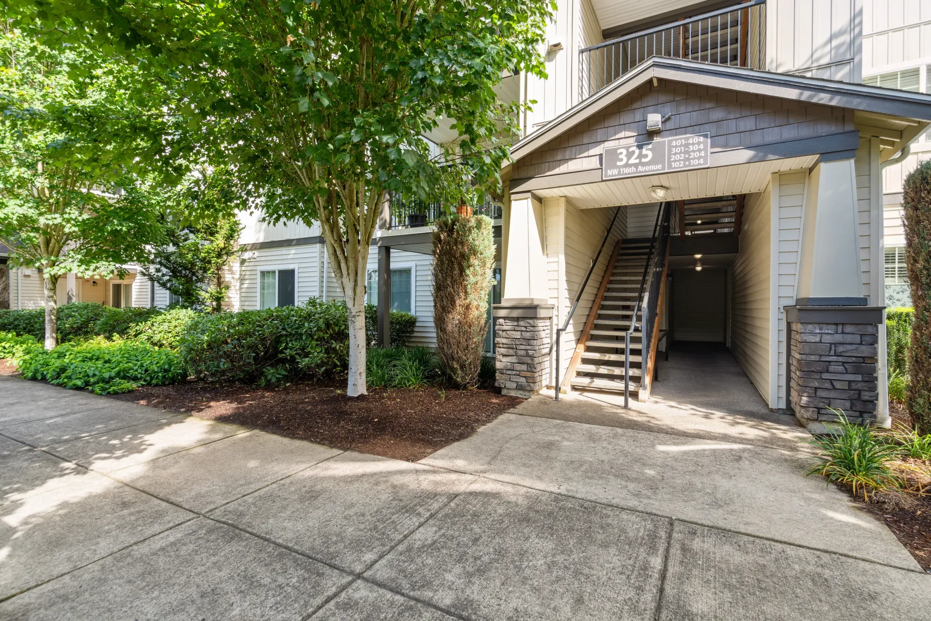 Exterior apartment building entrance with stairs and landscaping.