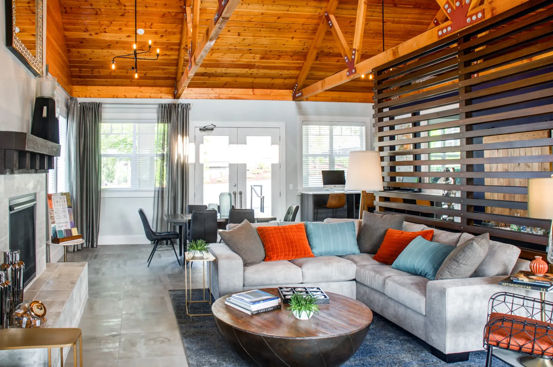Open-concept living room in an apartment with a gray sectional, round coffee table, fireplace, and exposed wooden beams.