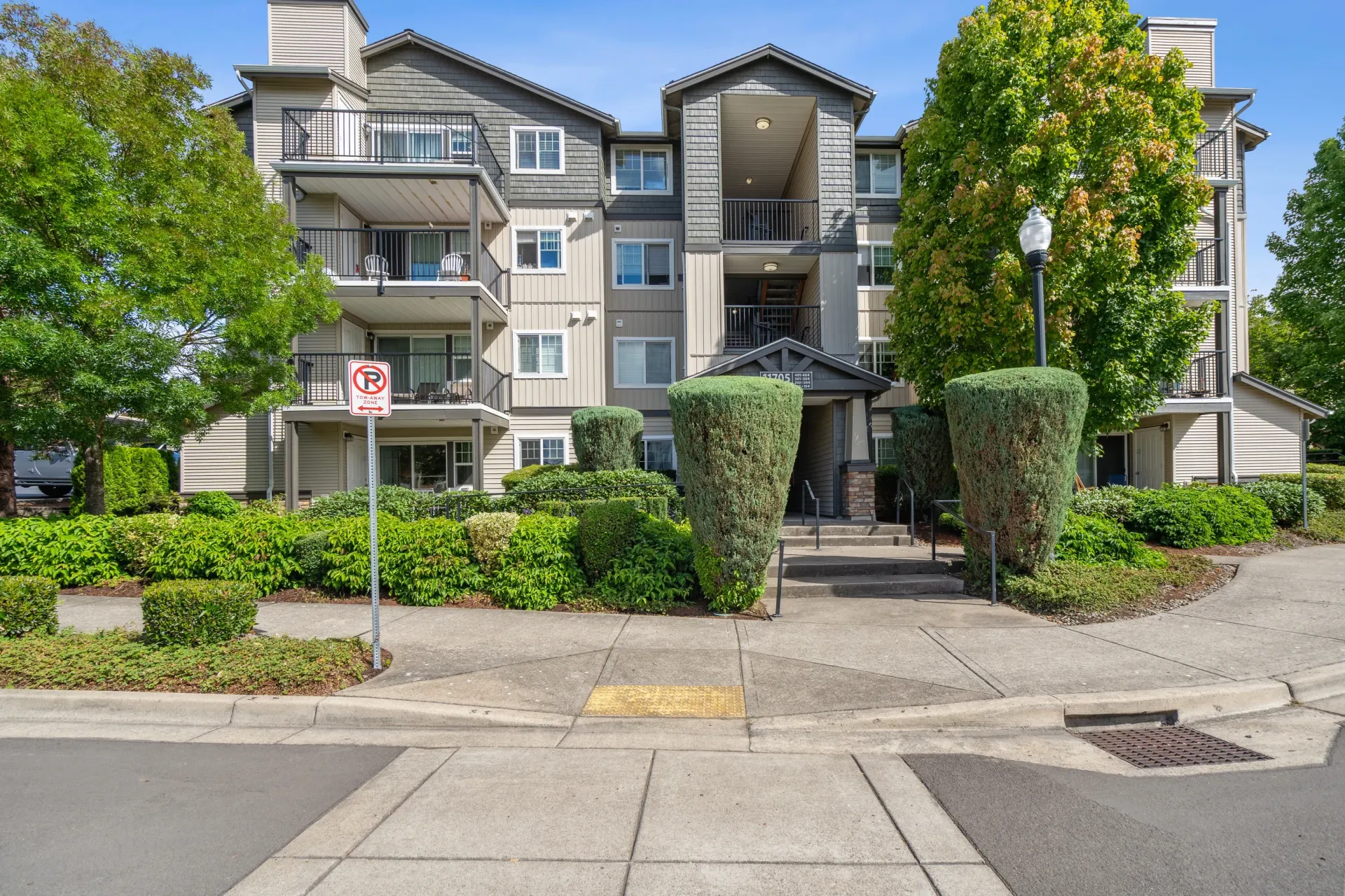 Exterior view of a multi-story apartment building with balconies and a landscaped entrance.