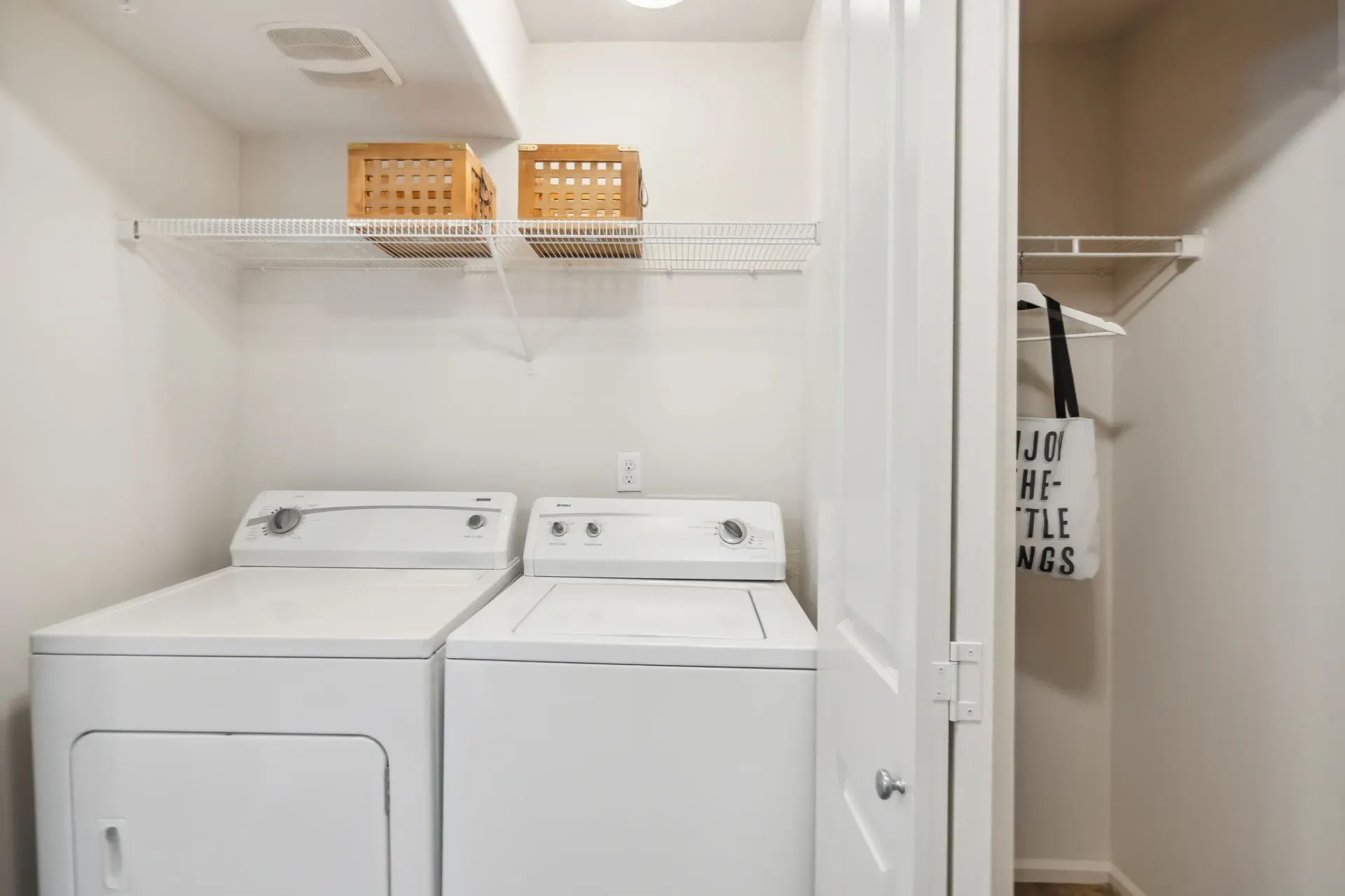 Laundry closet with a washer and dryer, white shelves, and storage baskets.