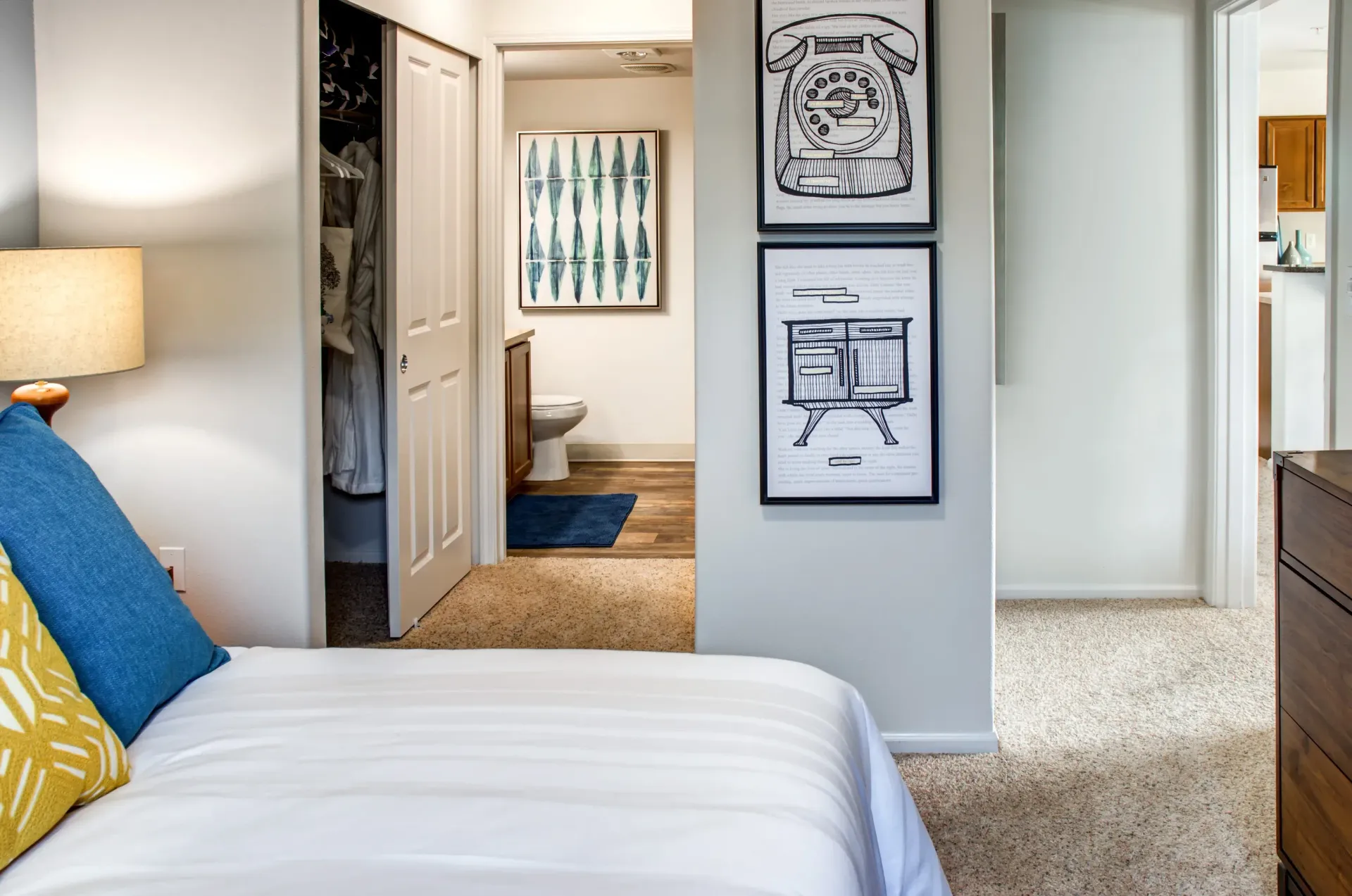 Bedroom interior with bed in foreground, open closet, and bathroom doorway with framed art.