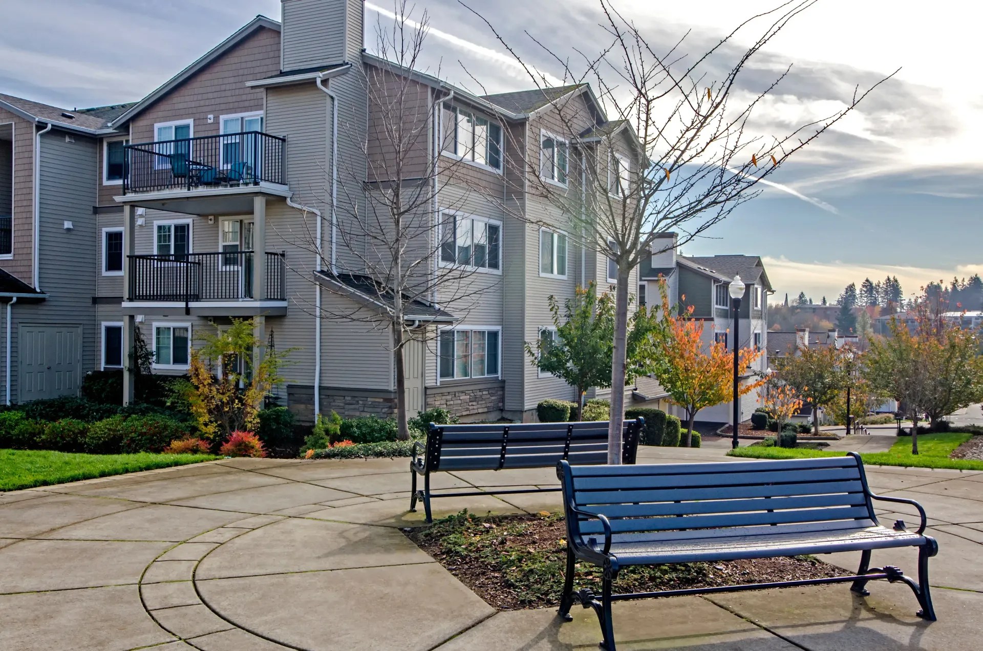 Exterior view of a multifamily apartment building with balconies, benches, and a curved walkway.