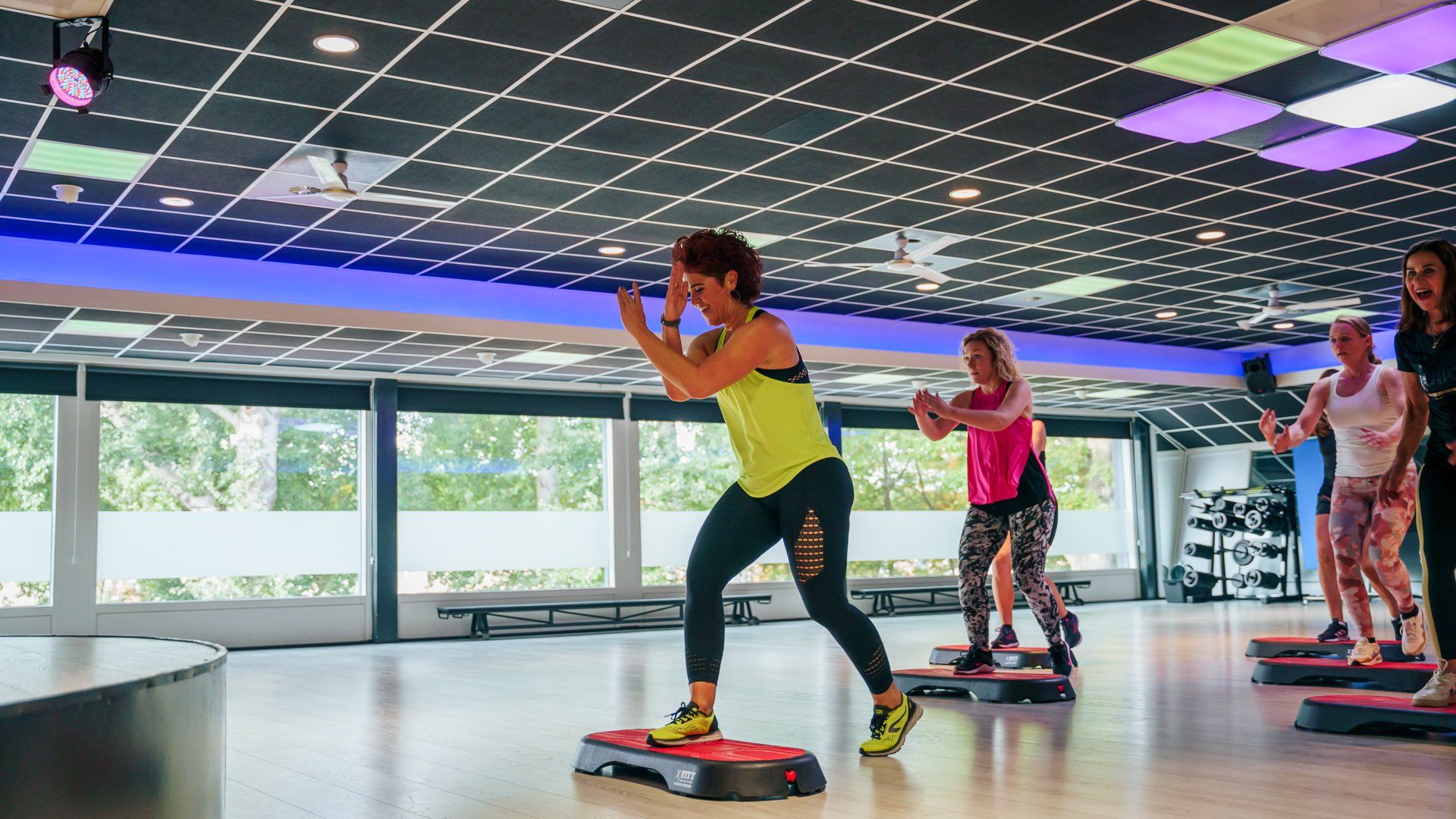 Mensen die step-aerobics doen in een lichte studio met kleurrijke plafondverlichting.