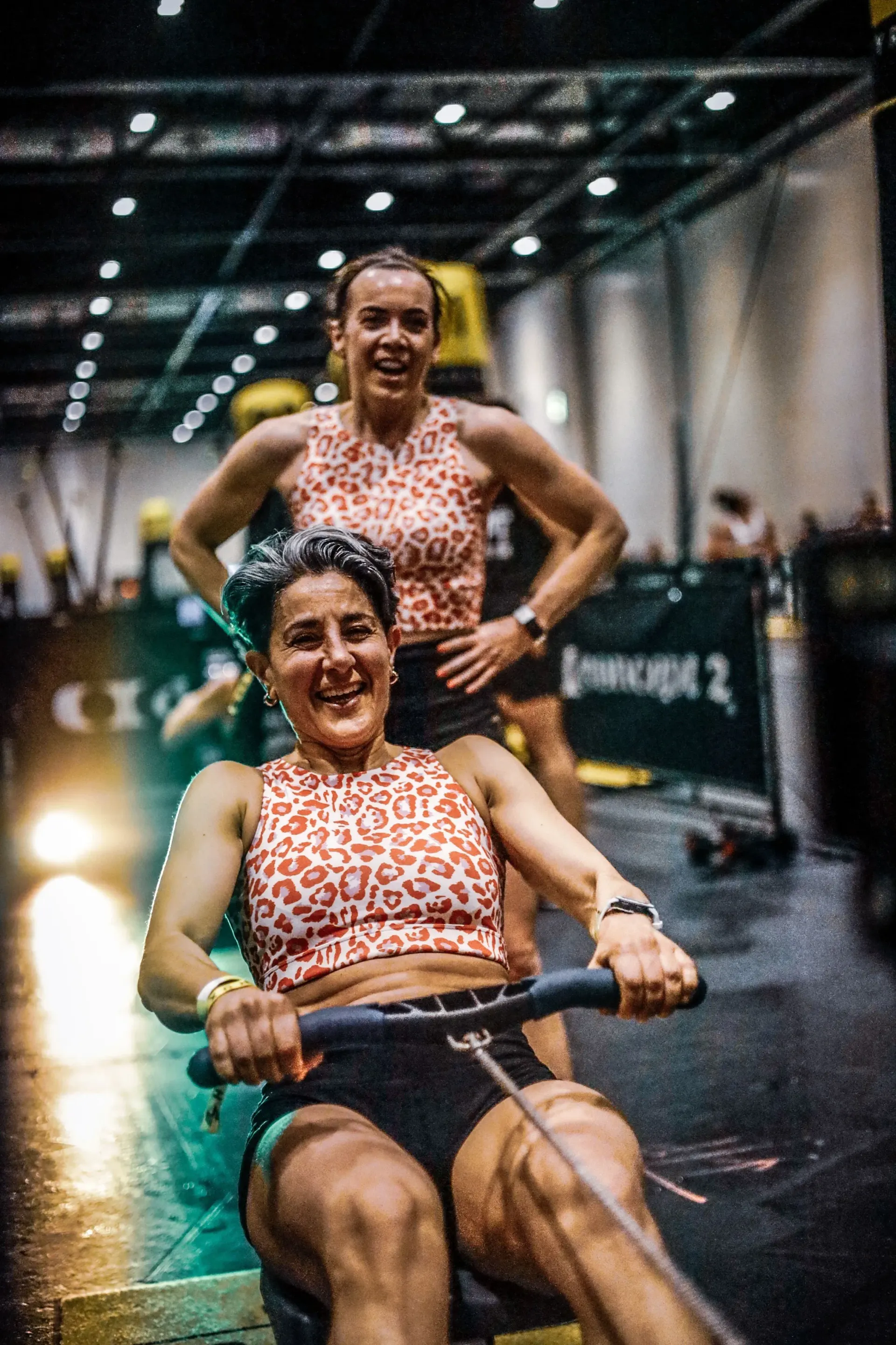 Twee vrouwen roeien op een apparaat in een sportschool.