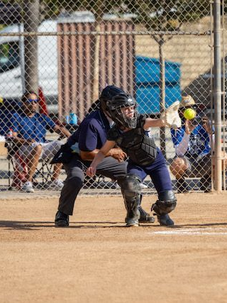 Softball catcher in uniform, catching the ball behind home plate at a daytime game.