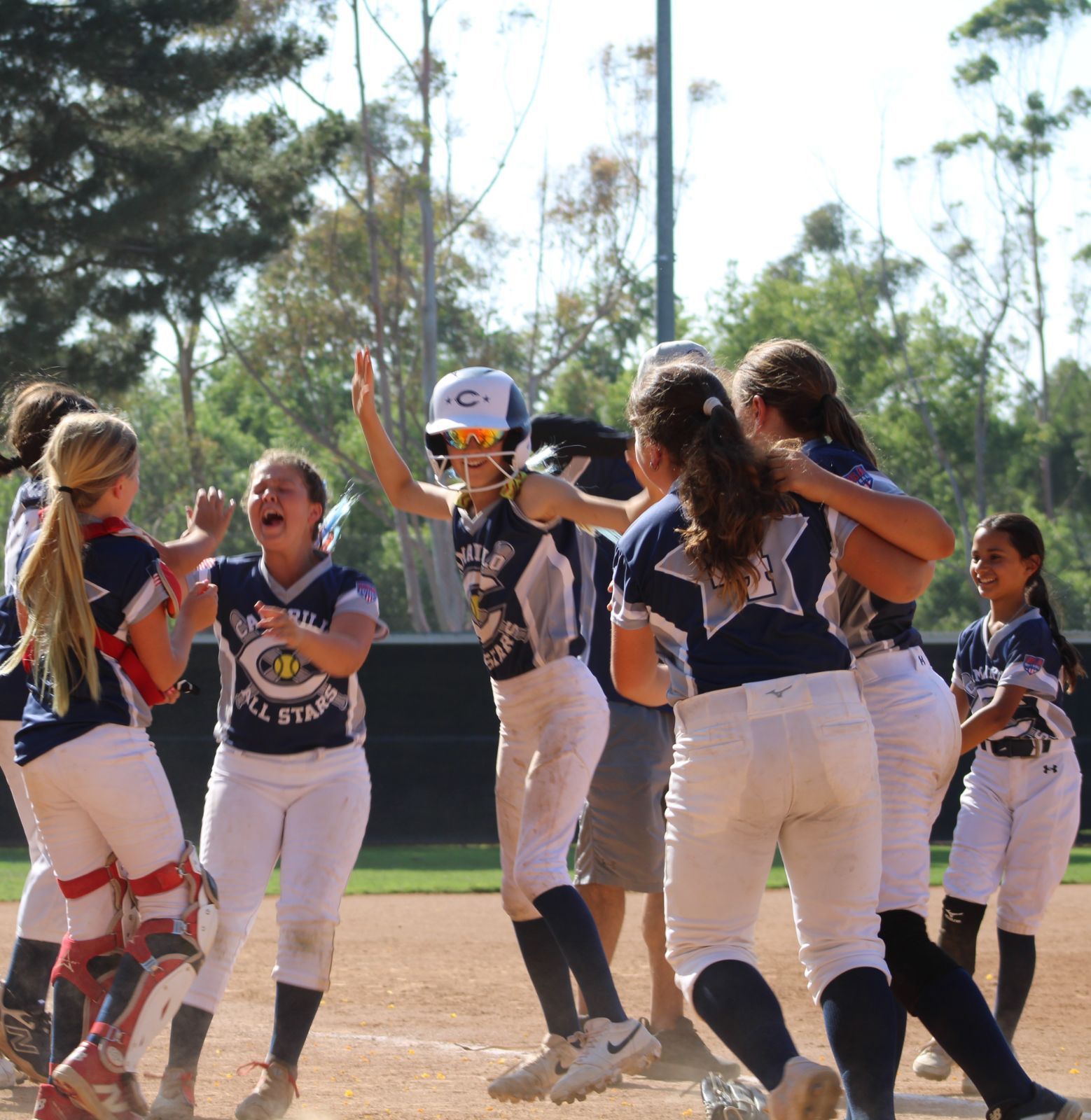 Softball team in navy and white uniforms celebrates on the field, arms raised in excitement.