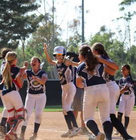 Softball team in navy and white uniforms celebrates on the field, arms raised in excitement.