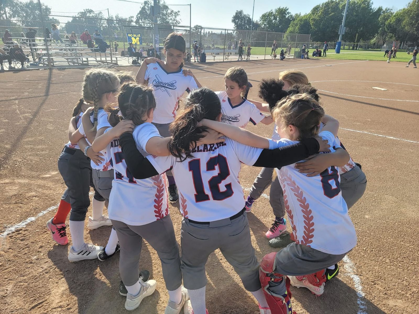 Softball team huddled together on a baseball field in team uniforms.