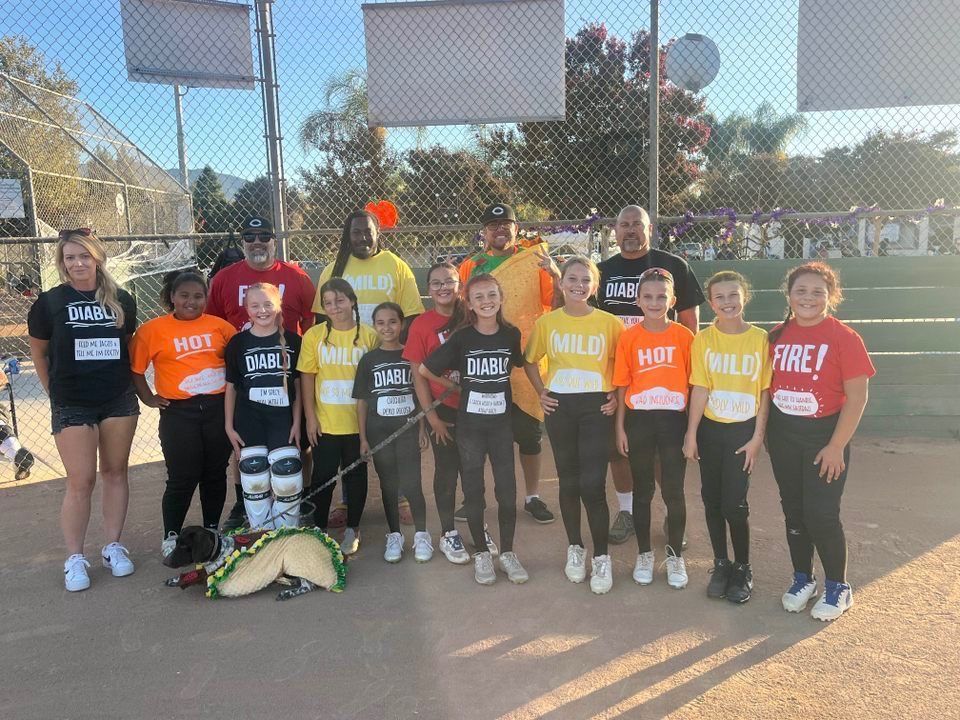 Group of people in team shirts pose on a baseball field. Some hold signs, including a dog in a costume.