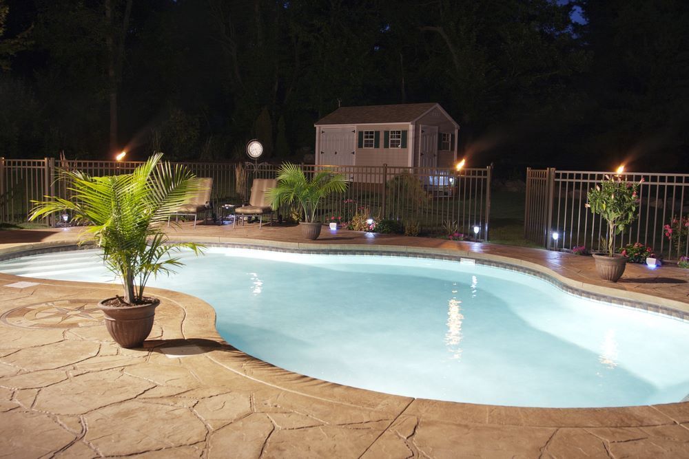 A Large Swimming Pool is Lit Up at Night — Top Shelf Glass Pool Fencing & Balustrading in Beenleigh, QLD