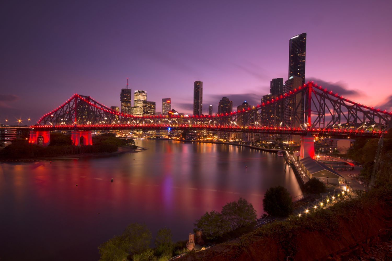 A Bridge Over a Body of Water With a City in the Background at Night — Top Shelf Glass Pool Fencing & Balustrading in Brisbane, QLD