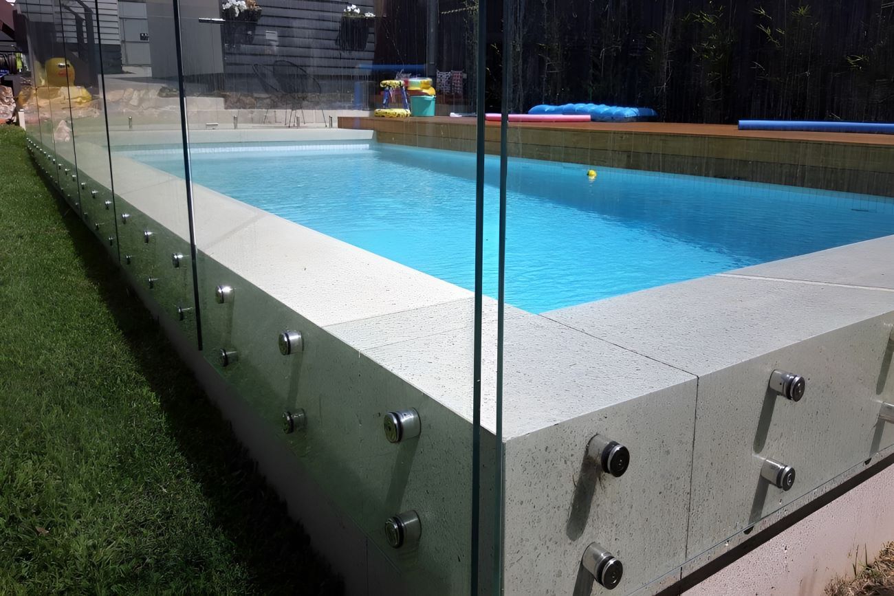 A Swimming Pool With a Glass Fence Around It — Top Shelf Glass Pool Fencing & Balustrading in Merrimac, QLD