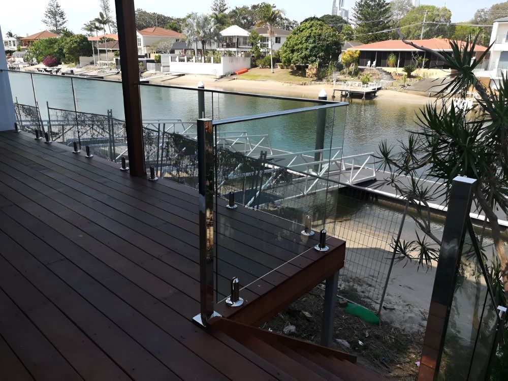 A Wooden Deck With a Glass Railing Overlooking a Body of Water — Top Shelf Glass Pool Fencing & Balustrading in Merrimac, QLD