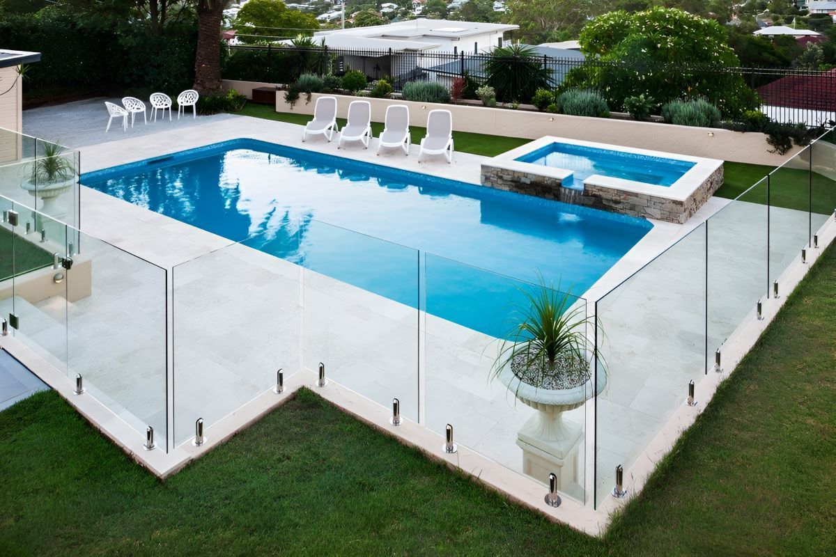 A Large Swimming Pool With a Glass Fence Around Chairs and Trees — Top Shelf Glass Pool Fencing & Balustrading in Tweed Heads, QLD
