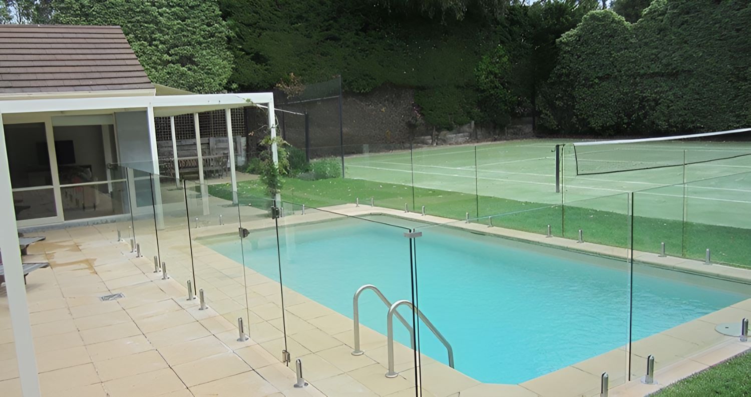 A Swimming Pool With a Glass Fence Around It and a Tennis Court — Top Shelf Glass Pool Fencing & Balustrading in Tweed Heads, QLD