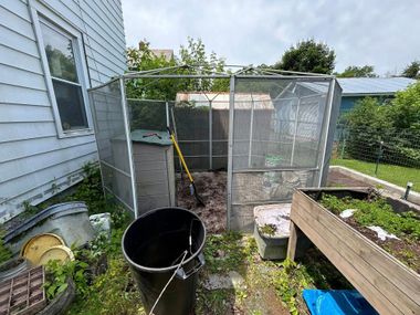Backyard garden area with raised beds, a wire enclosure, compost bin, and a yellow-handled shovel.