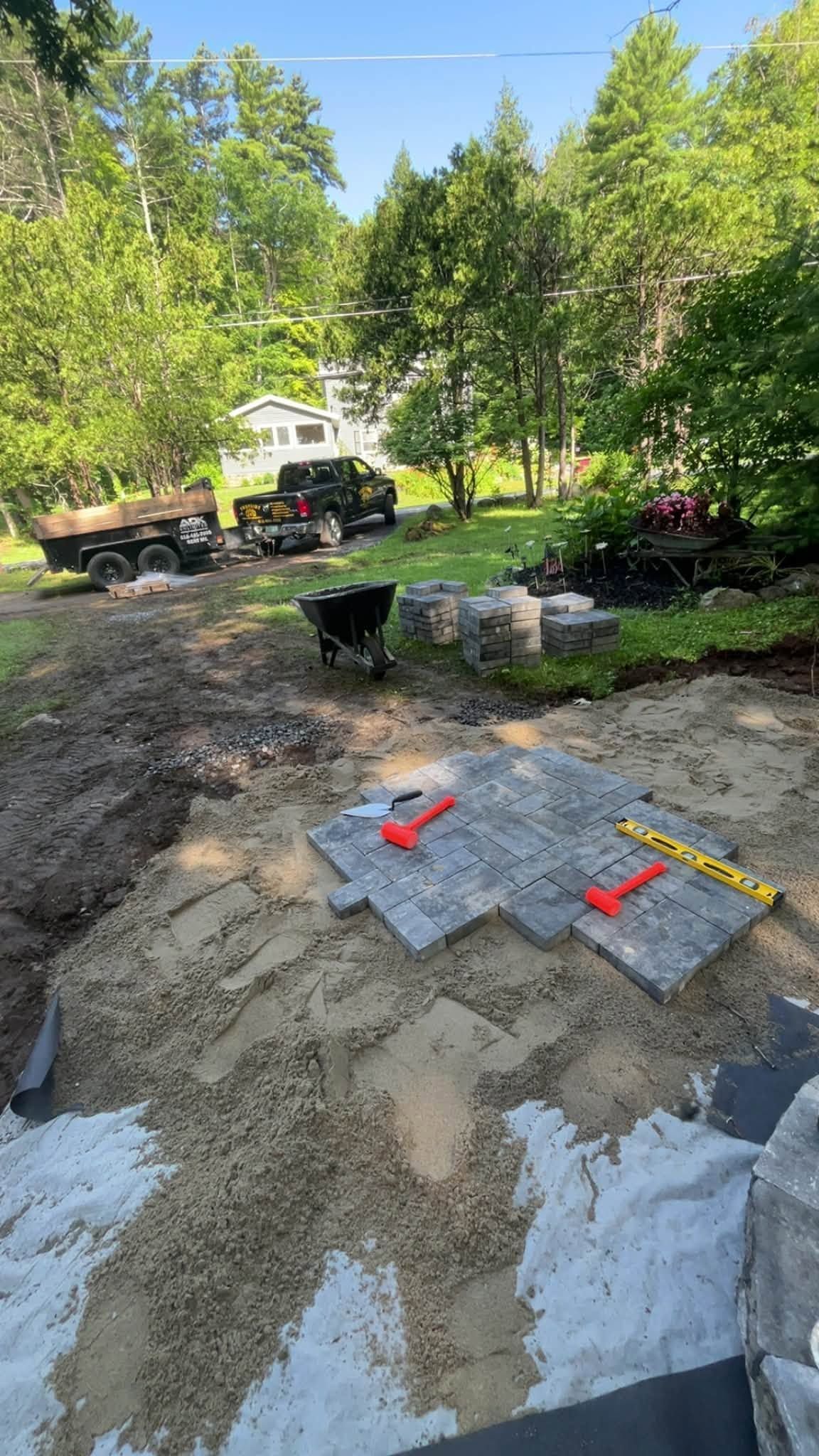 Construction site with gravel, red tools, and a worker near a truck among trees