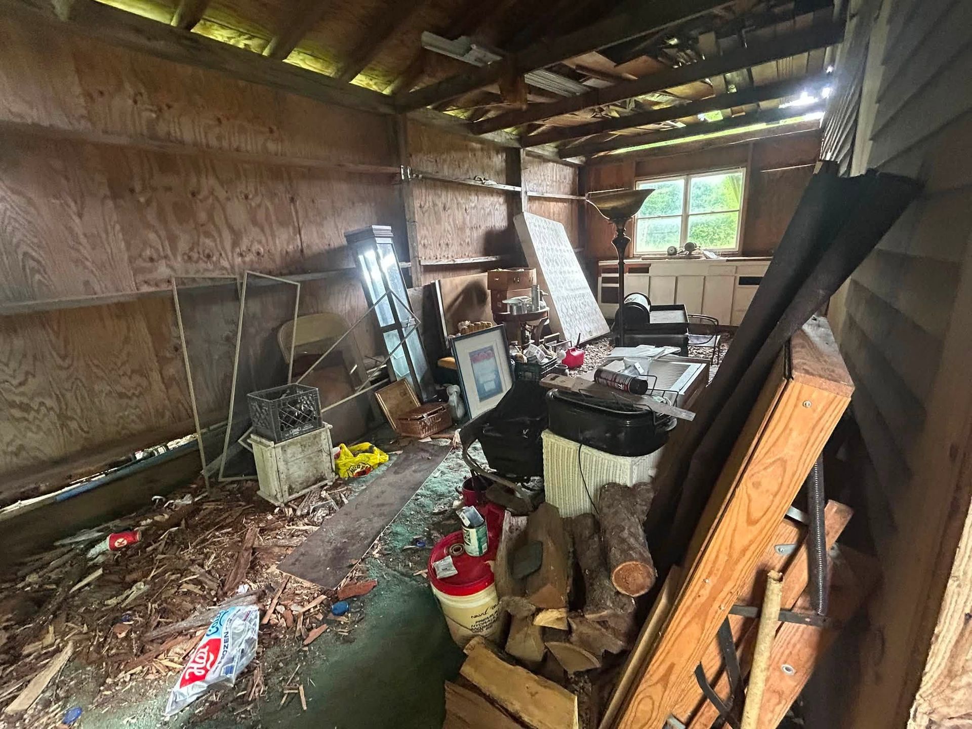 Cluttered, damaged room with debris, tools, and a broken wall under a sagging roof.