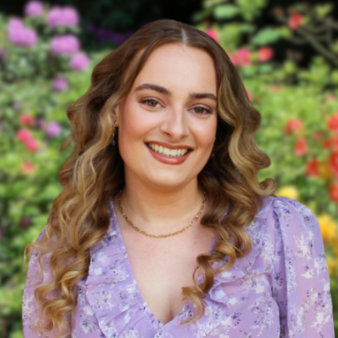 Een vrouw in een blouse en een ketting lacht naar de camera.