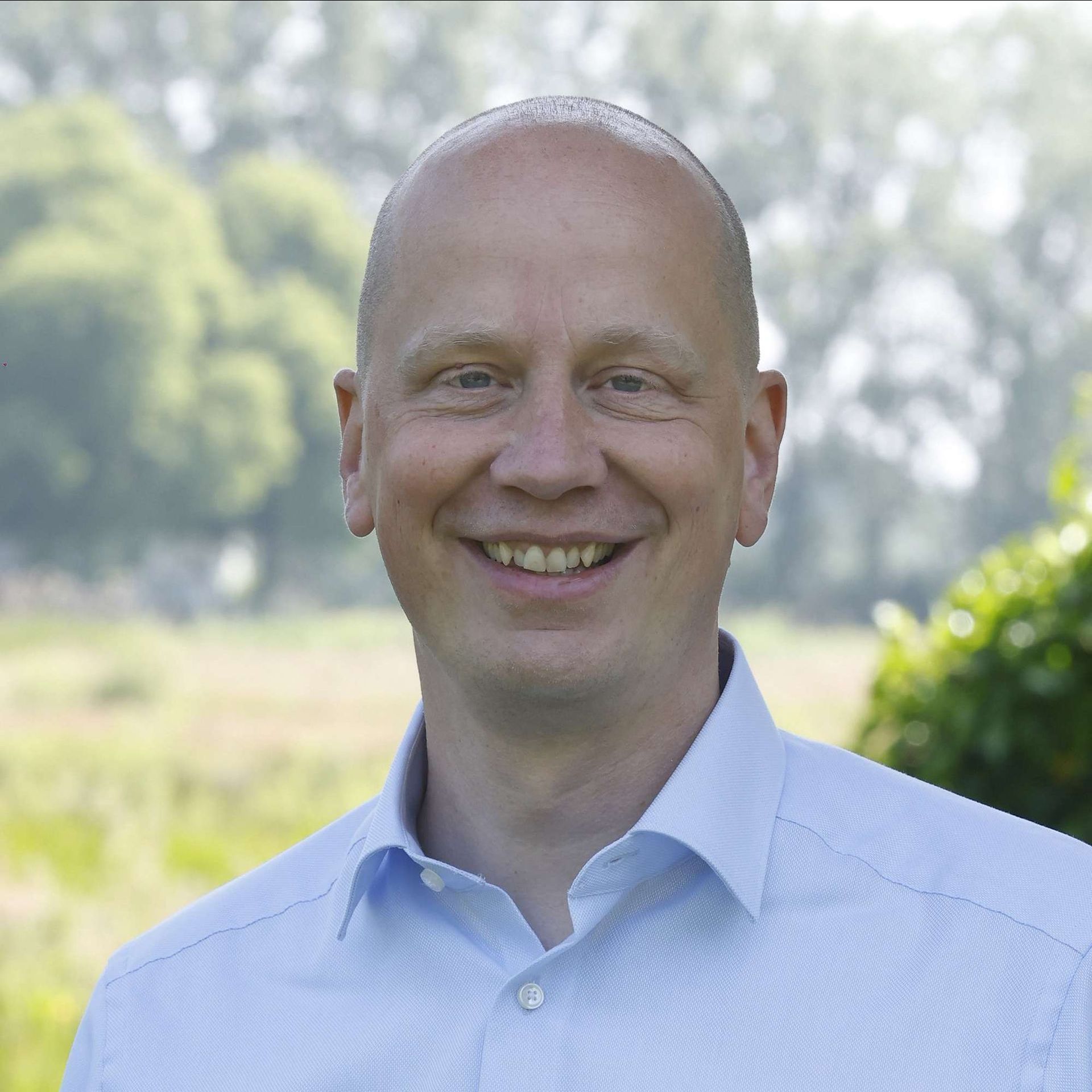 Een kale man in een blauw shirt lacht naar de camera