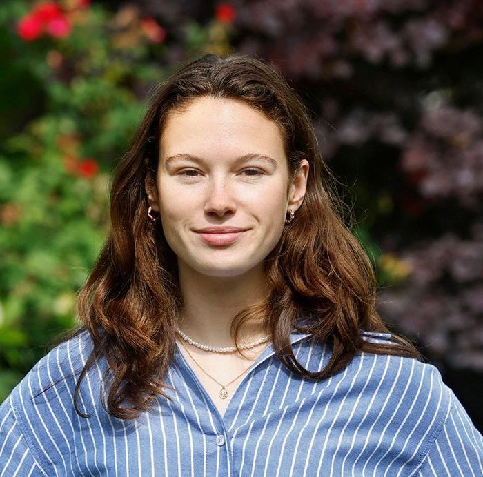 Een vrouw in een blauw-wit gestreept shirt lacht naar de camera.