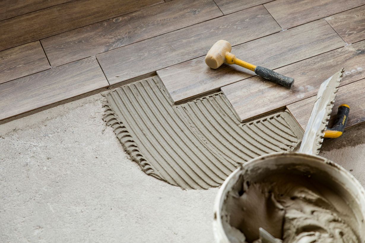 Un martello e un secchio di colla sono appoggiati su un pavimento di legno.