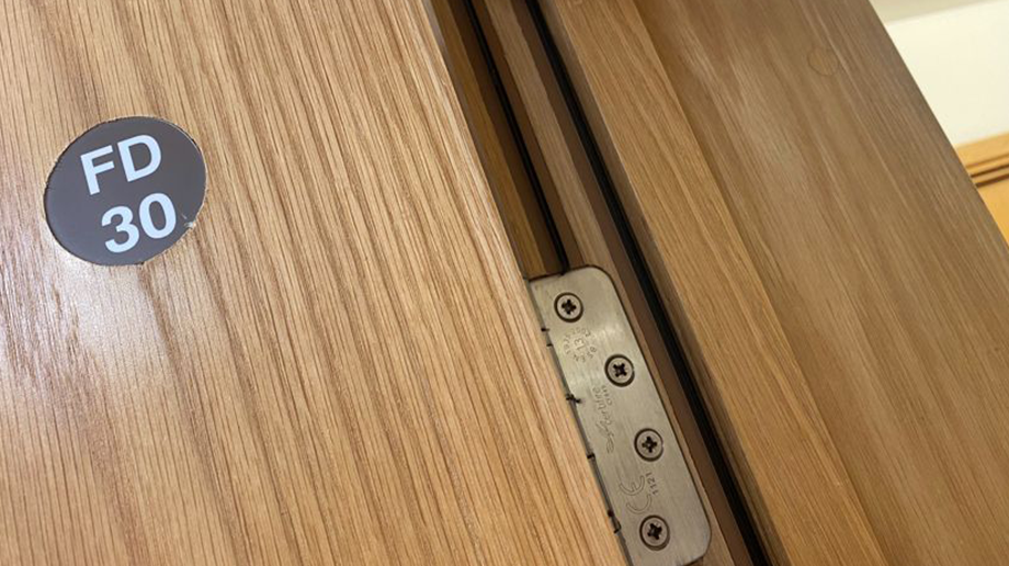 Close-up of a certified FD30 fire door with visible rating sticker and compliant intumescent hinge detailing.