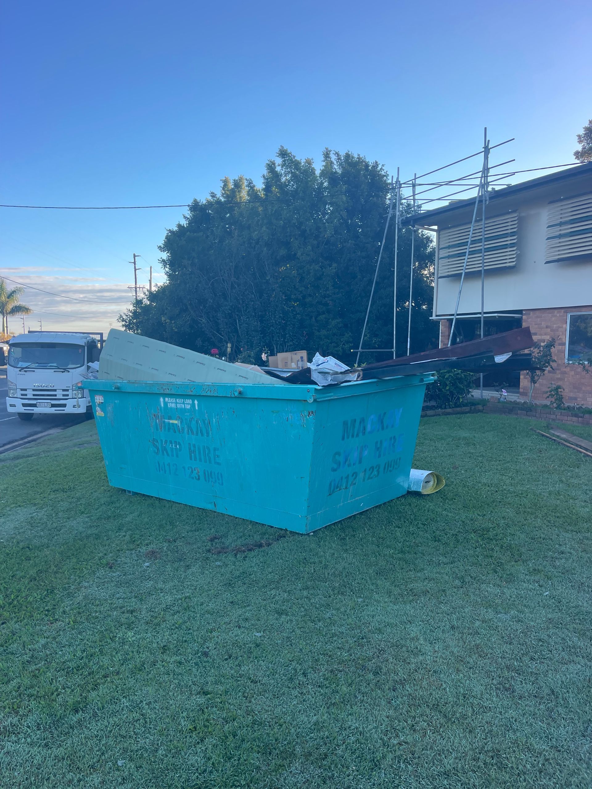 A Large Turquoise Dumpster on a Lawn, Overflowing — Mackay Skip Hire In Andergrove, QLD