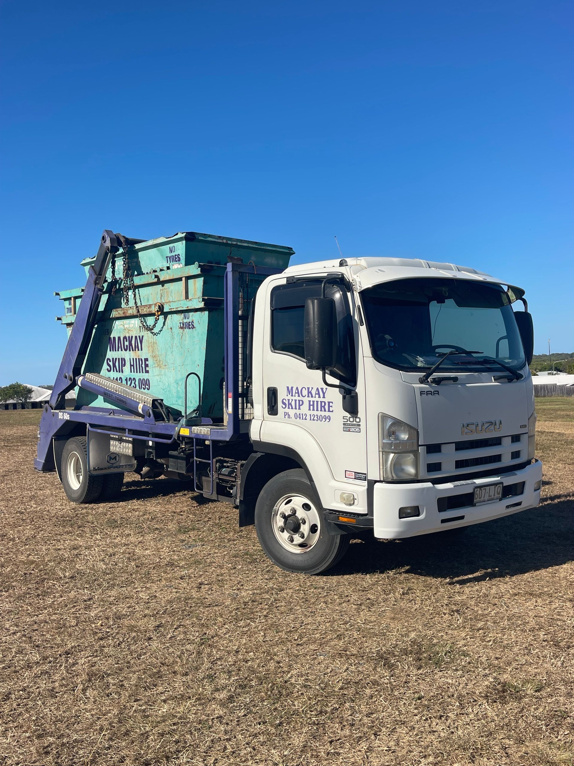 White Isuzu Skip Bin Truck With Blue Skip Against a Blue Sky — Mackay Skip Hire In Andergrove, QLD
