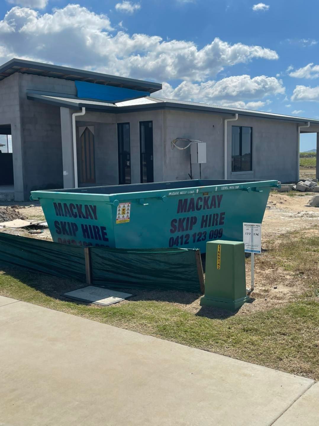 Green Skip Bin in Front of a House Under Construction; Cloudy Sky — Mackay Skip Hire In Andergrove, QLD