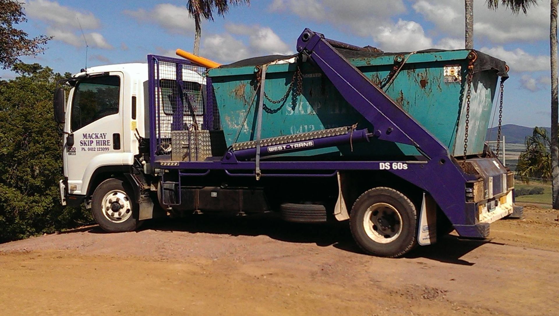 Red Dumpster Filled With Demolition Debris in Front of a House, Portable Toilet Nearby — Mackay Skip Hire In Andergrove, QLD