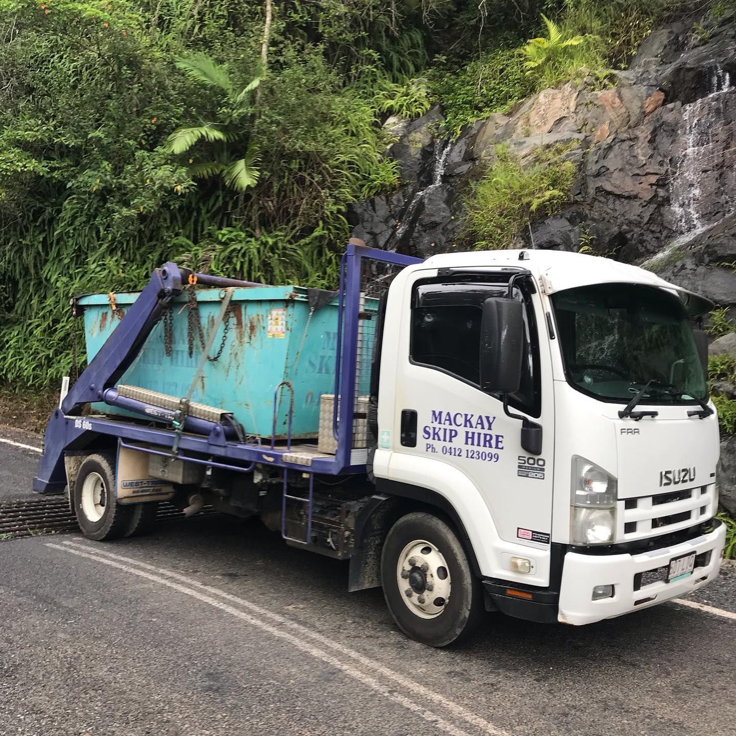 White Isuzu Truck With a Blue Skip Bin on a Road — Mackay Skip Hire In Andergrove, QLD