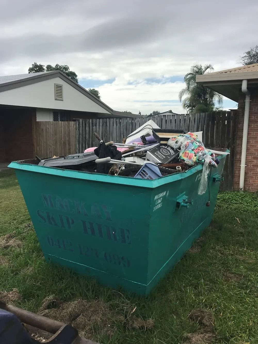 Green Dumpster Filled With Trash Sits on a Grassy Yard — Mackay Skip Hire In Andergrove, QLD