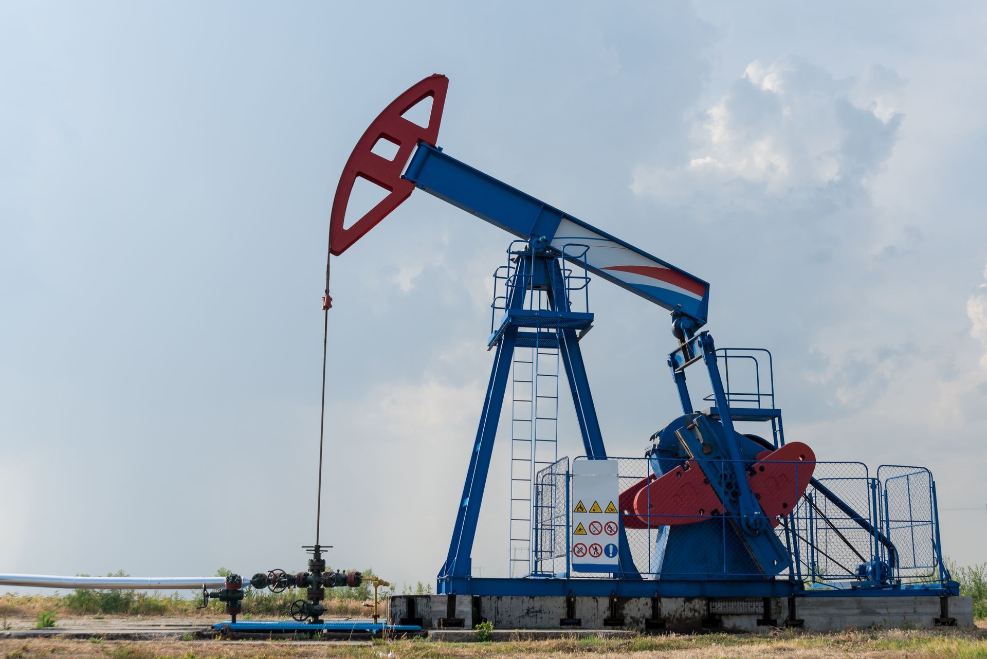 A blue and red pumpjack operates in a field under a cloudy sky.