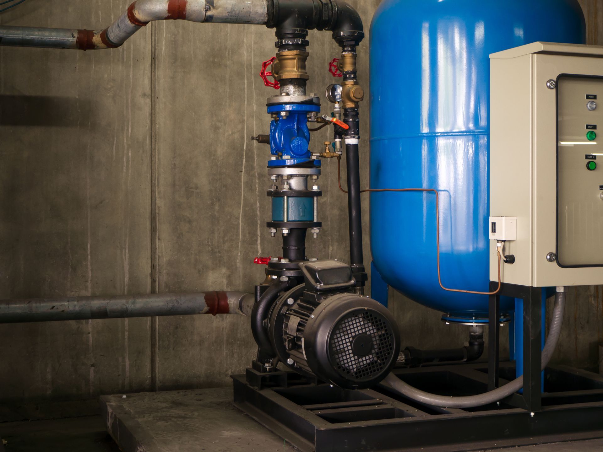 A blue pressure tank, an electric water pump, and a control panel installed against a concrete wall.