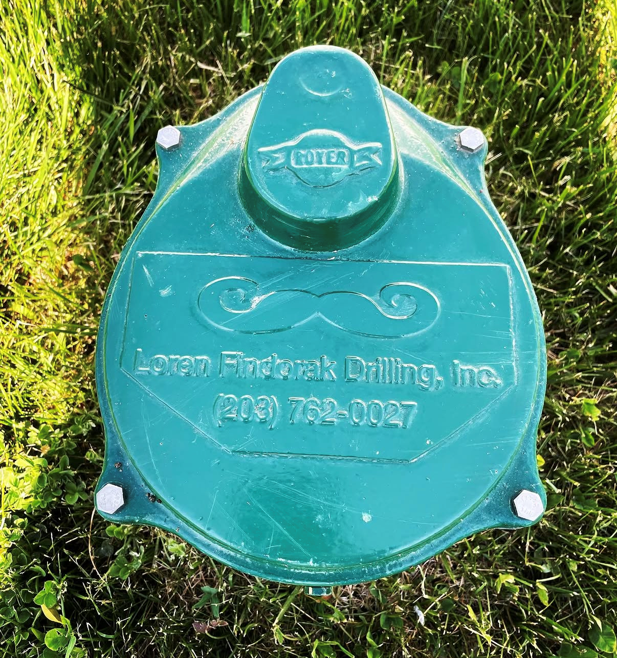 A person wearing work gloves connects a blue pipe to a white plumbing fixture near a large blue water pressure tank.