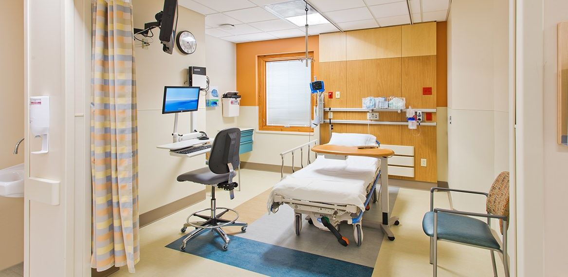 A hospital room with a bed , chairs , and a computer.