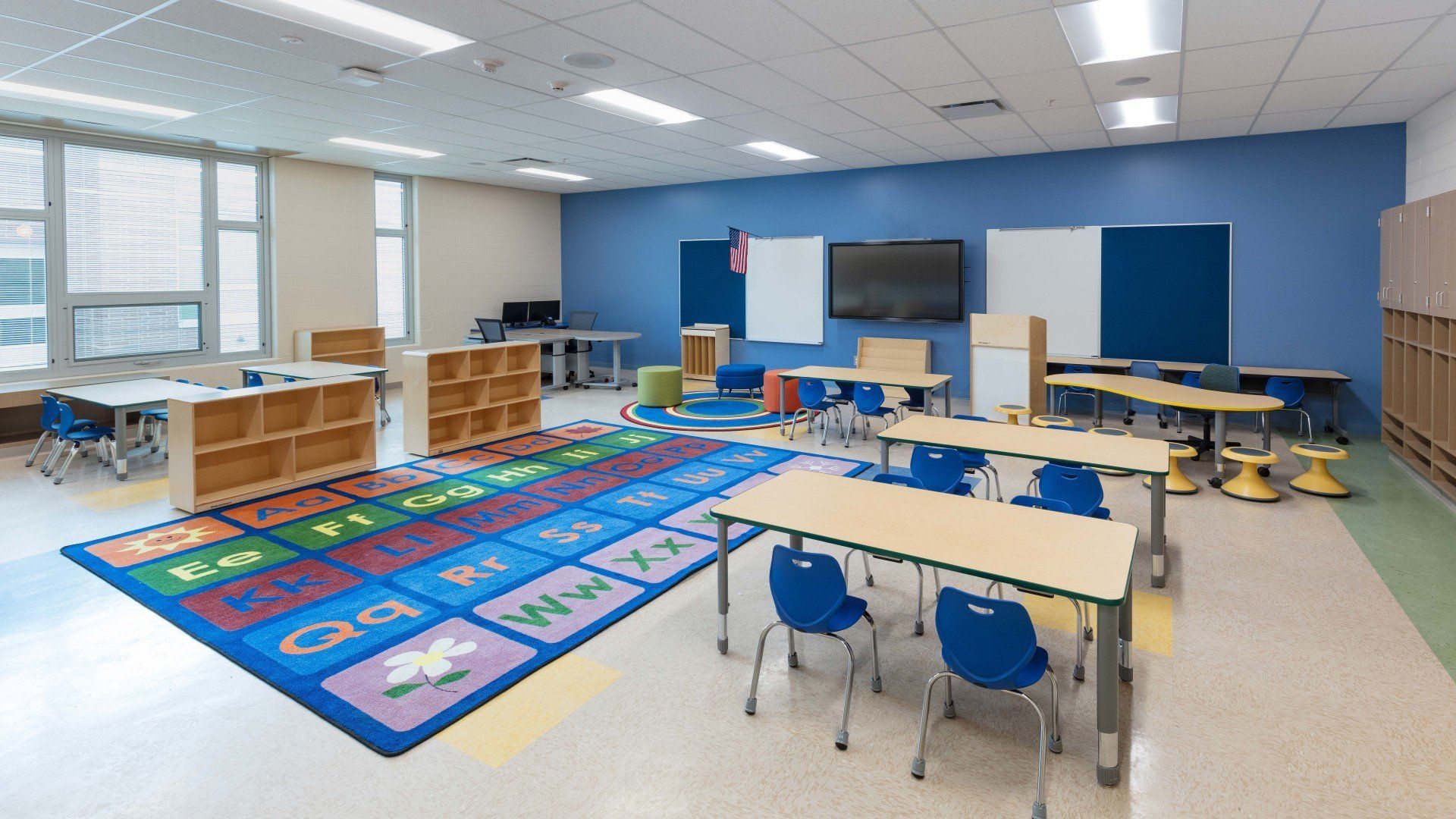 A classroom with tables and chairs and a rug on the floor.