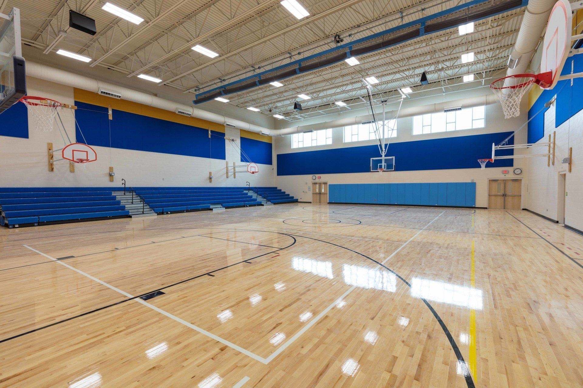 An empty basketball court with a wooden floor and a basketball hoop.