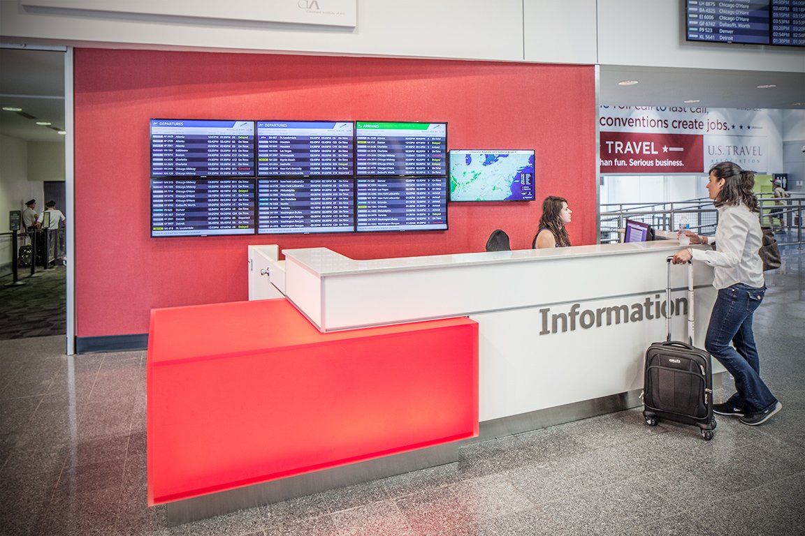 A woman is standing in front of a information desk at an airport.