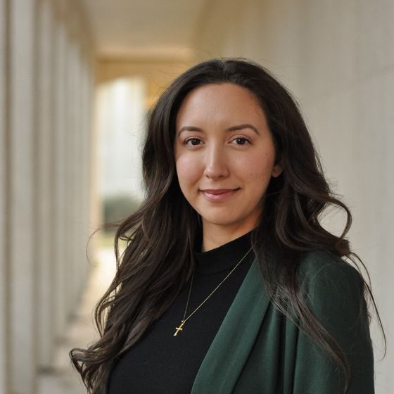 A woman wearing a black shirt and a green jacket is smiling for the camera