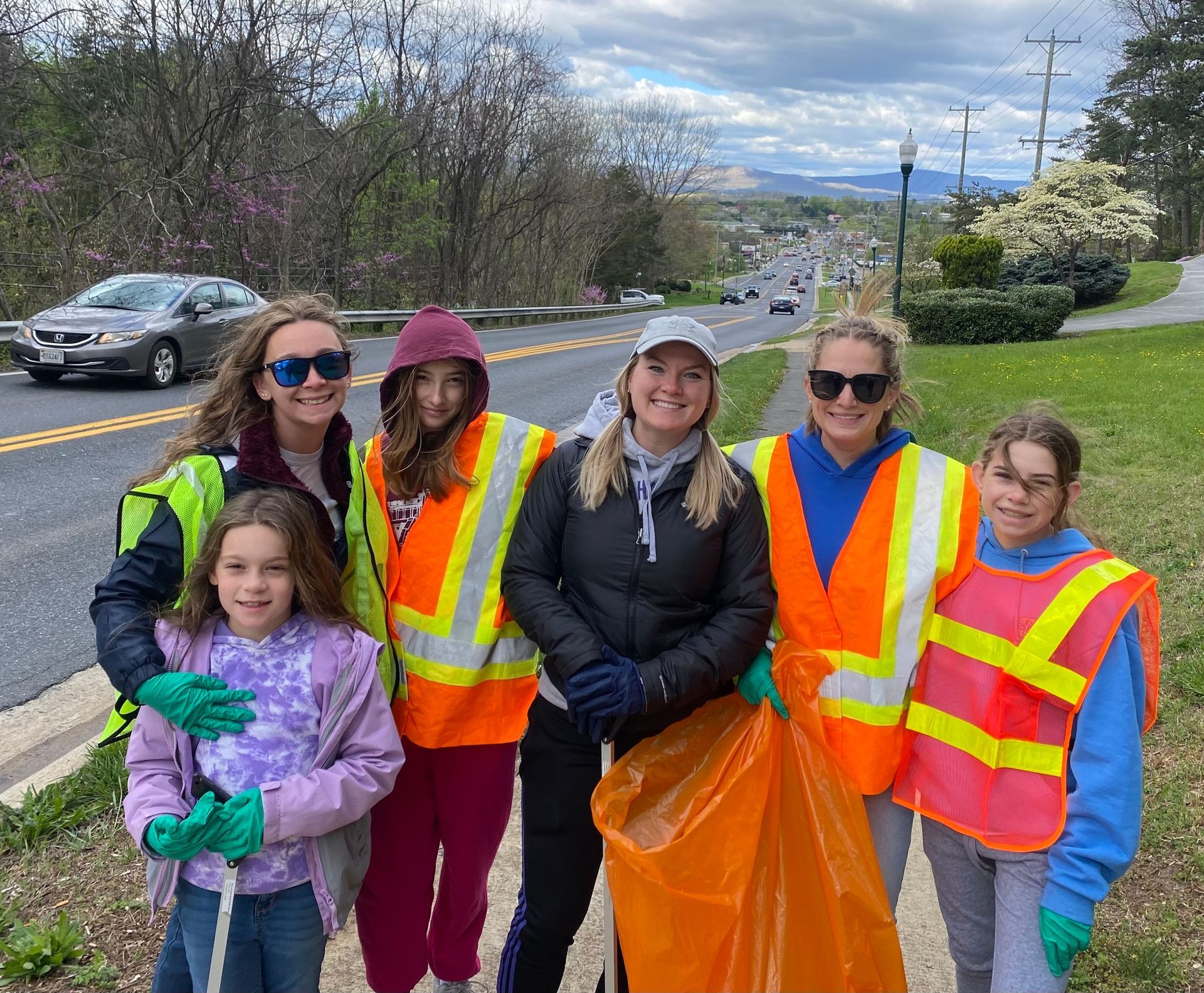 A group of rotarians and their daughters with safety vests and trash pickers alongside the adopted road.