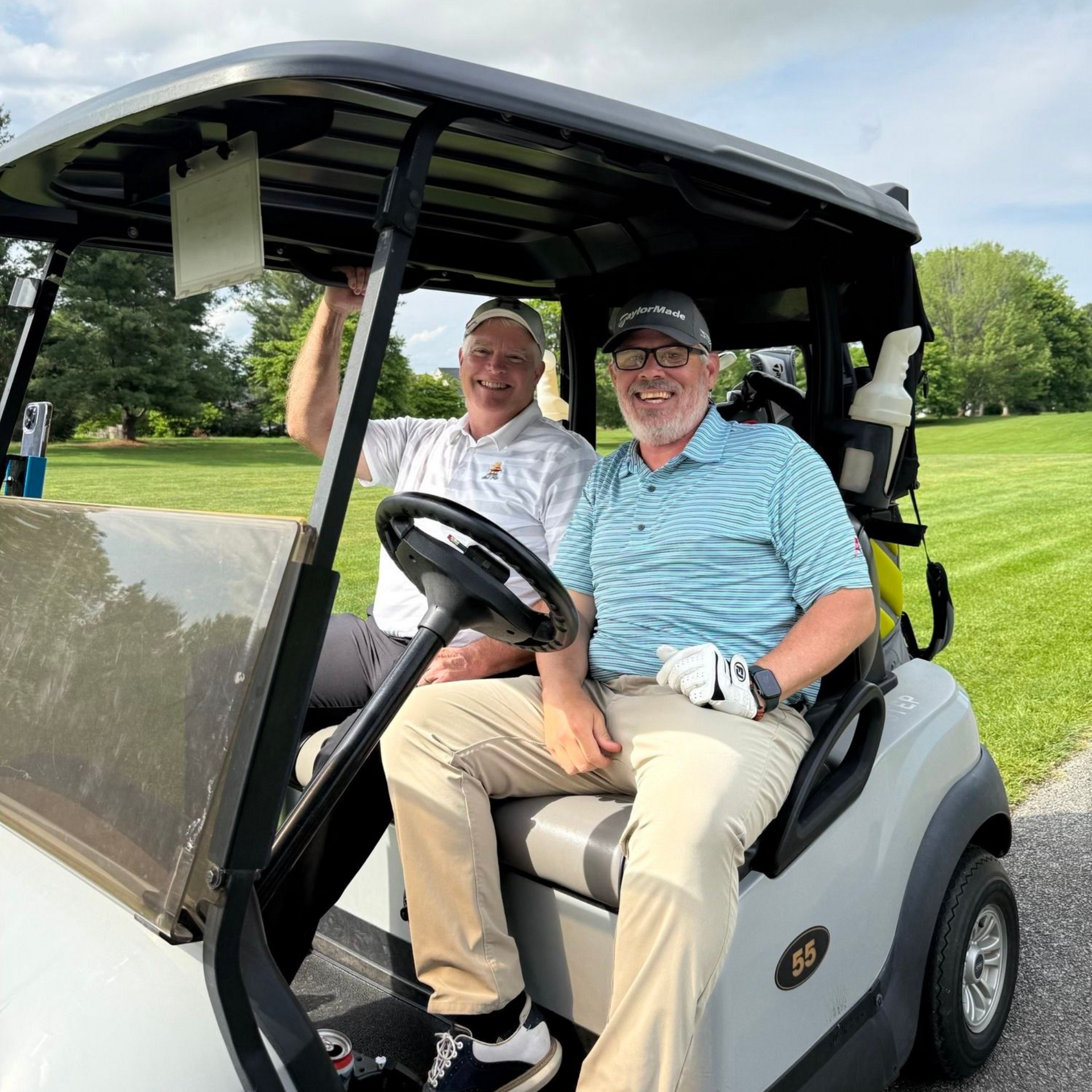 Two male golfers in a golf cart on the course.