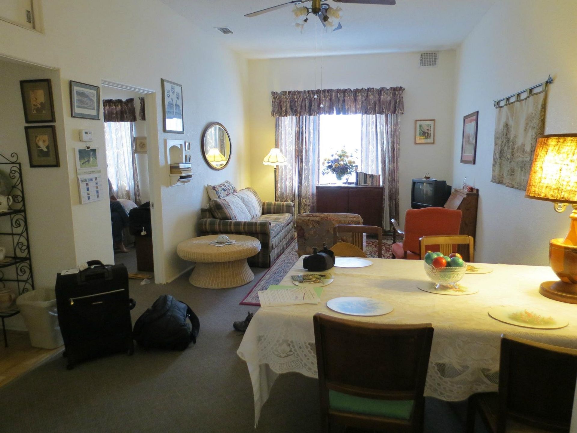 A living and dining room with a dining table in the foreground, a sofa in the back, and luggage on the carpeted floor.