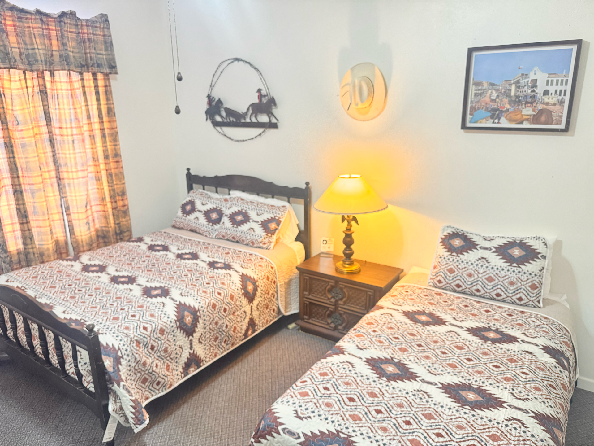 A bedroom with a red bedspread on a wooden bed frame, decorated with wall-mounted straw hats, under a ceiling fan.