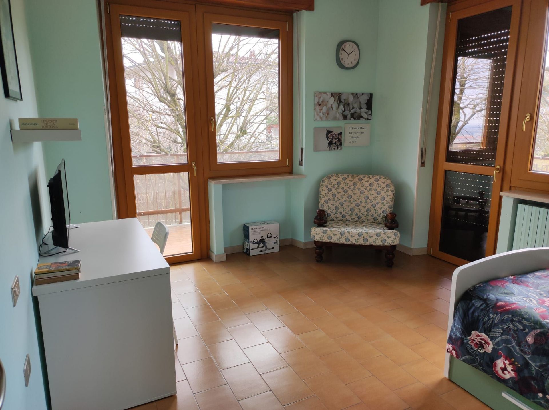 Una camera da letto con un letto, una sedia, una scrivania e un orologio sul muro.