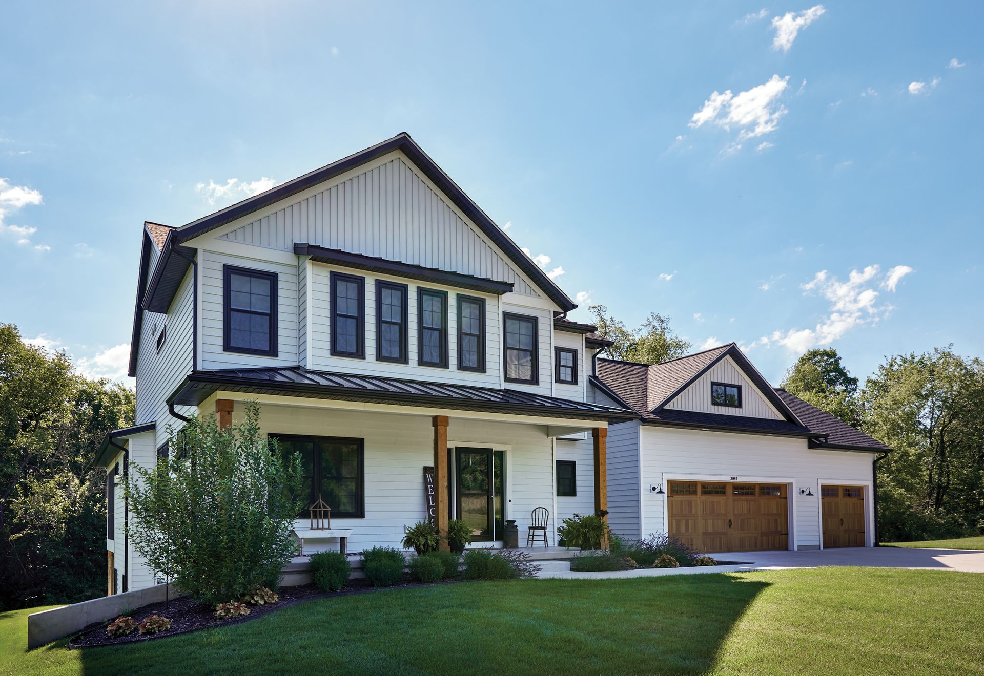 White farmhouse with black trim, two-car garage, and green lawn under a blue sky.